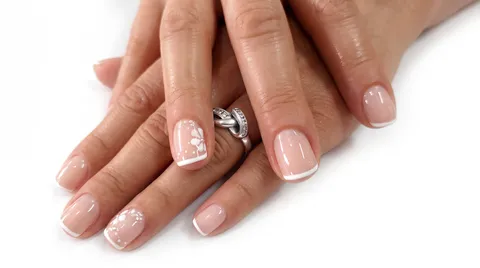 Manicure francesa suave con acento floral y pedrería en una uña