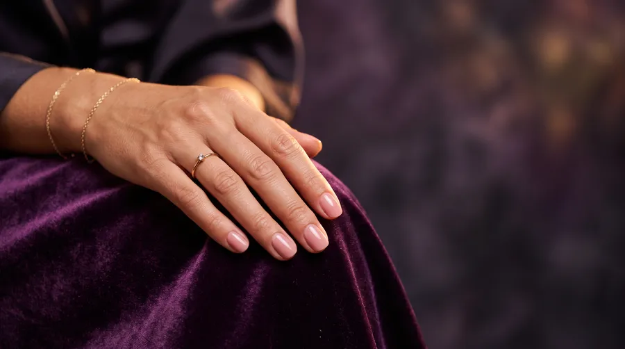 Mano con manicure semipermanente en tono nude apoyada sobre terciopelo morado, ambiente íntimo de spa